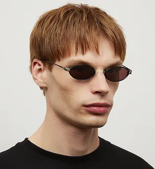 Young man with light brown hair wearing small oval dark sunglasses and a black shirt.